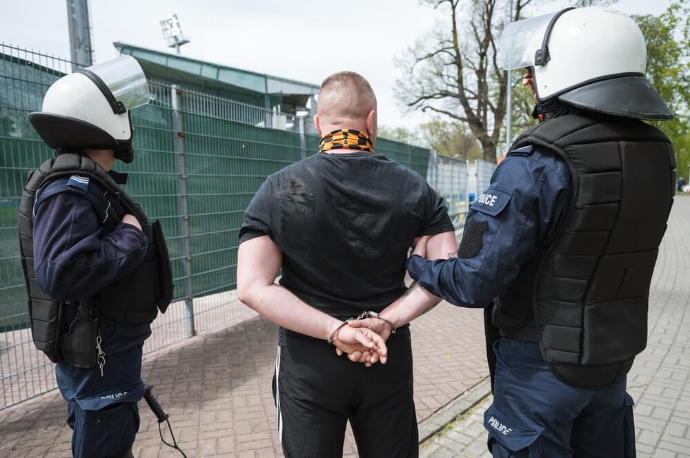 The policeman holds the detained man in handcuffs.